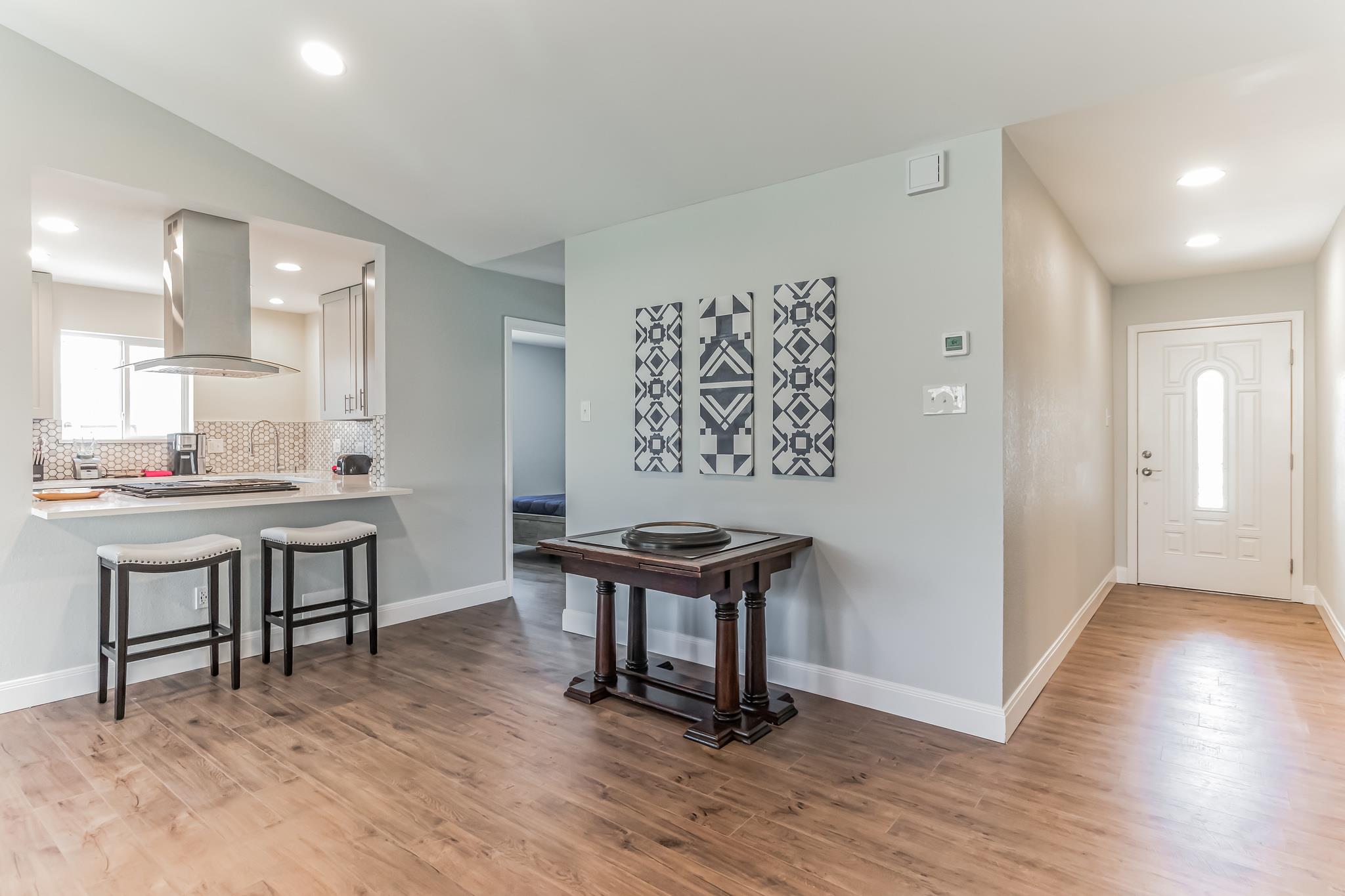 Open-plan kitchen and entry with wood floors, breakfast bar, and a game table beneath geometric wall art.