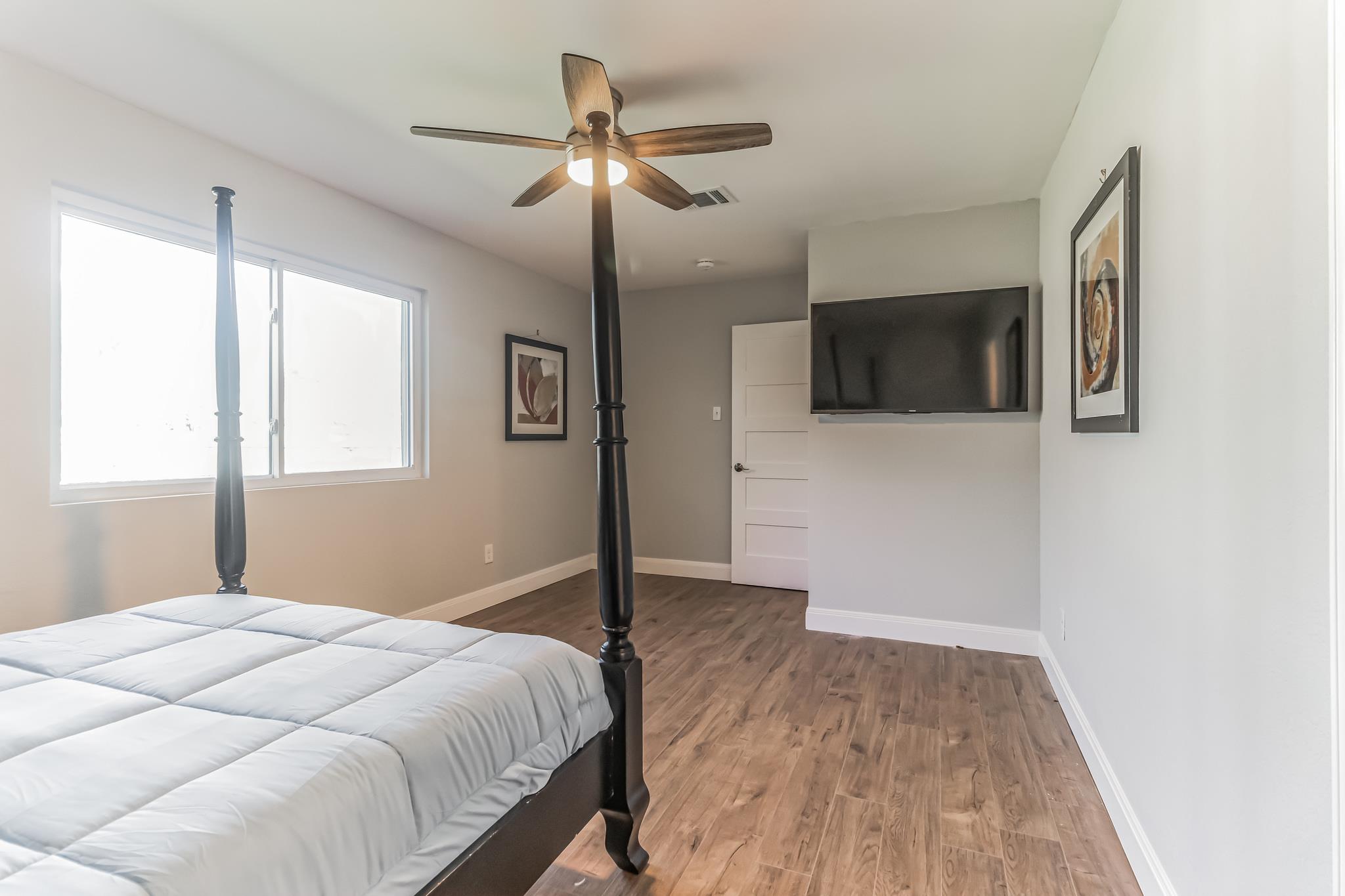 Bedroom with a dark four-poster bed, wood-look flooring, and a wall-mounted television.