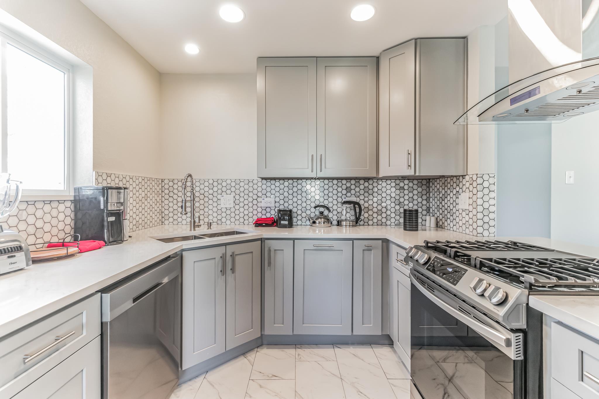 Kitchen with gray cabinets, hexagonal tile backsplash, farmhouse sink, and stainless steel gas range.