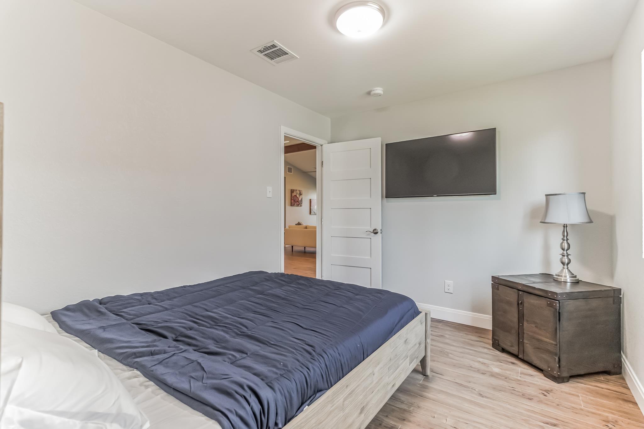 Bedroom with dark blue bedding, a wall-mounted TV, and a dark wood cabinet with a lamp.