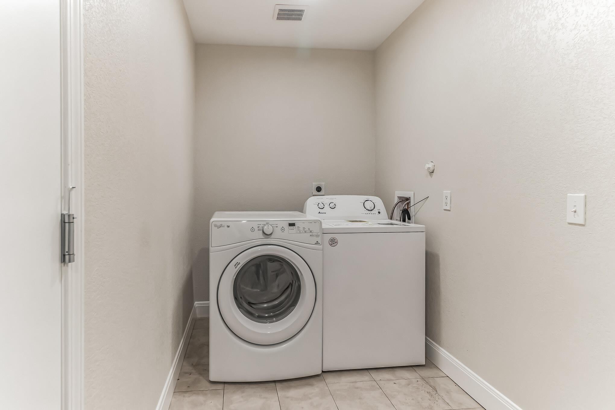 Laundry room with a front-loading dryer beside a top-loading washer and gray tile floor.