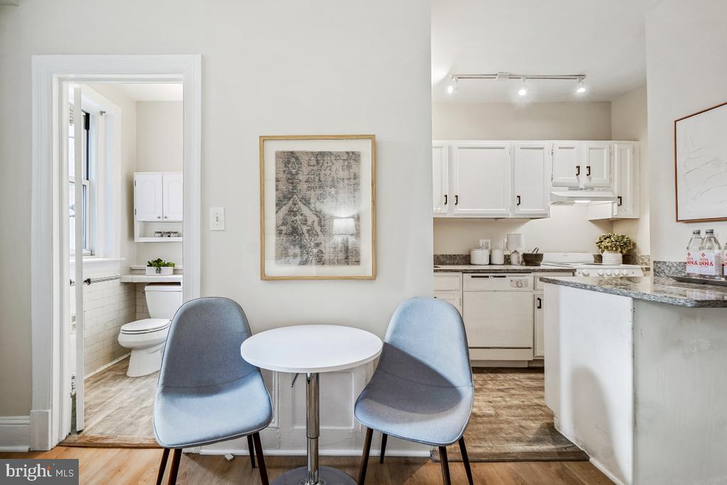 Dining nook with two blue chairs, open white kitchen, and bathroom doorway.