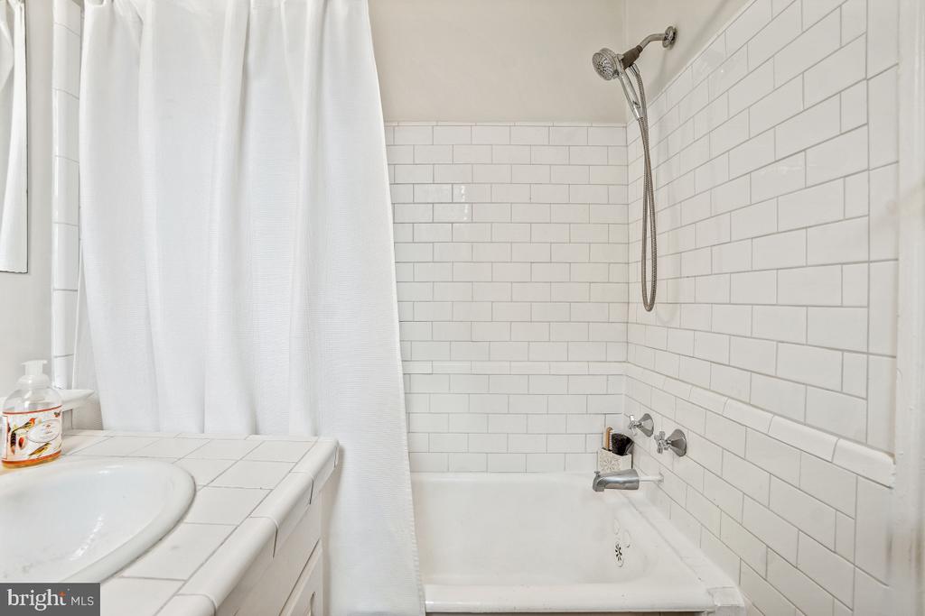 Bathroom with a white subway-tile tub surround, handheld showerhead, and tiled vanity.