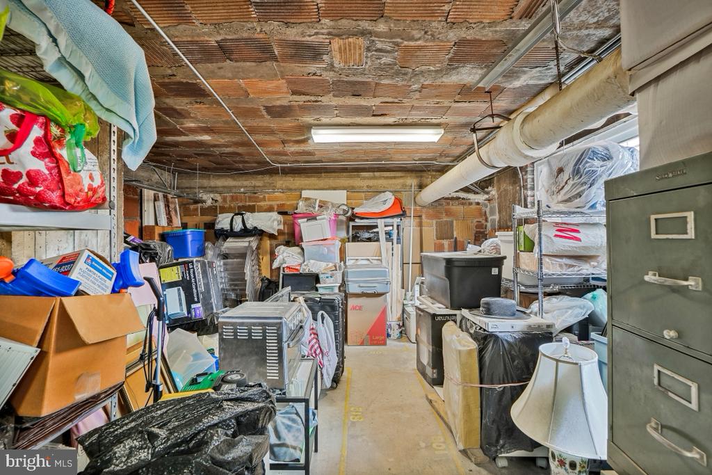 Basement storage room with an exposed brick ceiling, crowded shelves, boxes, and filing cabinets.