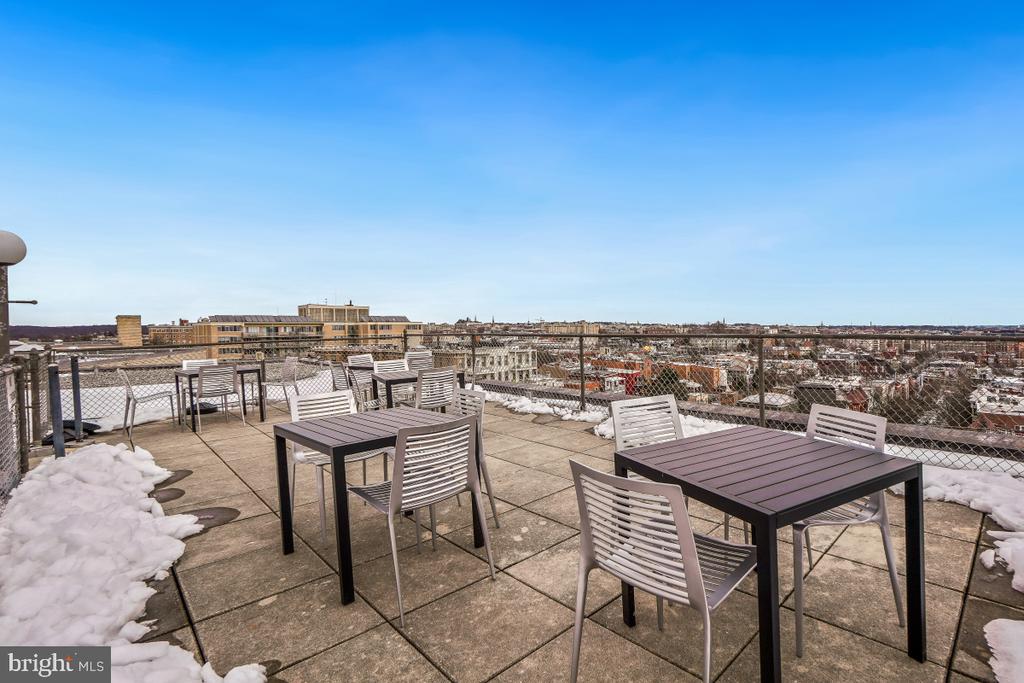 Rooftop terrace with patio tables, chairs, patches of snow, and a wide city view.