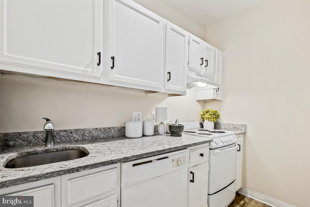 Compact kitchen with white cabinets, gray-speckled counters, a stainless sink, and a white electric range.