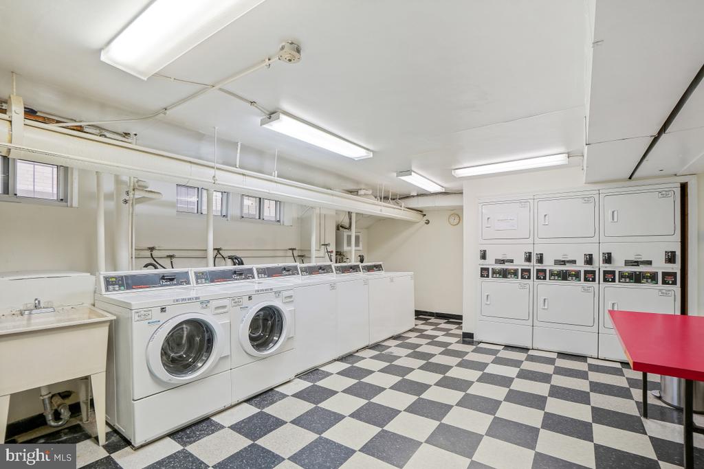 Shared laundry room with front-loading washers, stacked dryers, and checkerboard flooring.