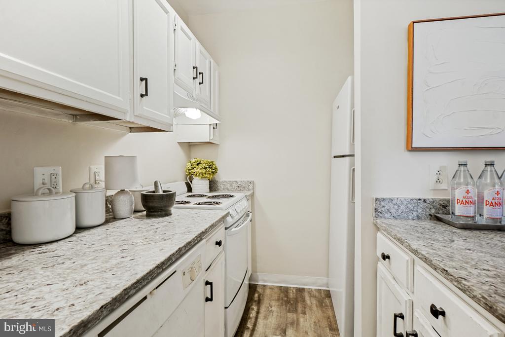 Staged kitchen with white cabinetry, speckled stone counters, and wood-look flooring.