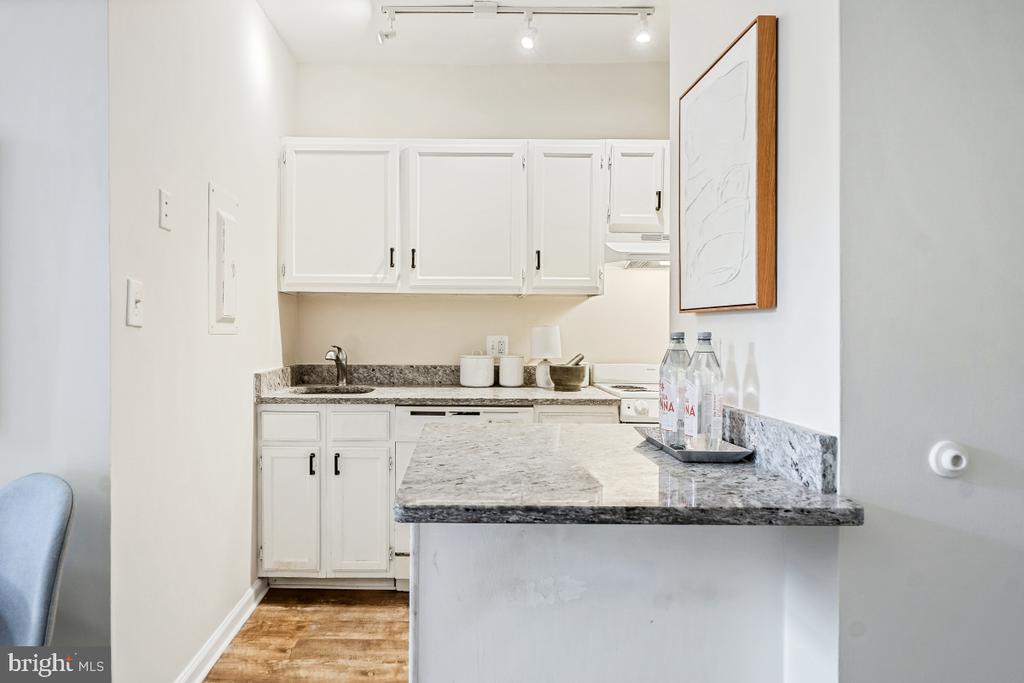 White kitchen with paneled cabinets, gray stone counters, and a breakfast bar.