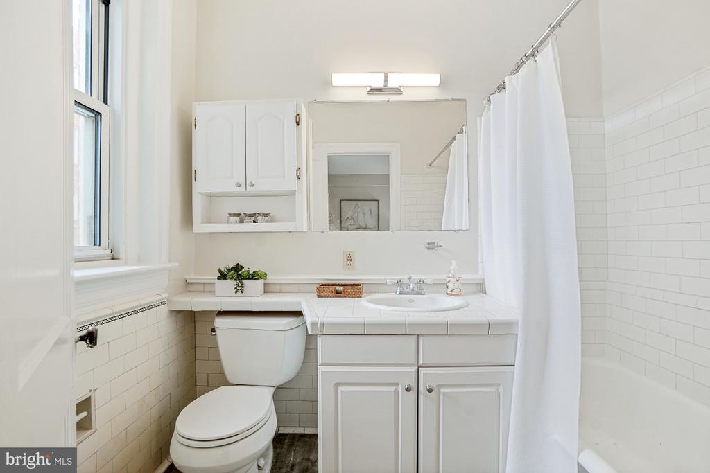 Bathroom with white tiled walls, a shower curtain, and a vanity beneath a large mirror.