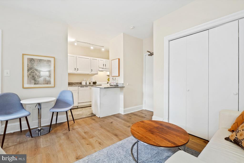 Studio living area with a compact white kitchen, blue dining chairs, and sliding closet doors.