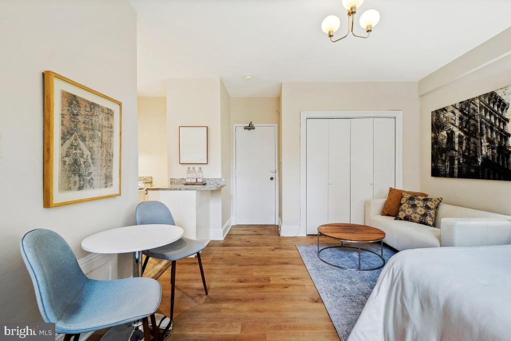 Furnished studio apartment with a bed, white sofa, dining nook, and wood floors.
