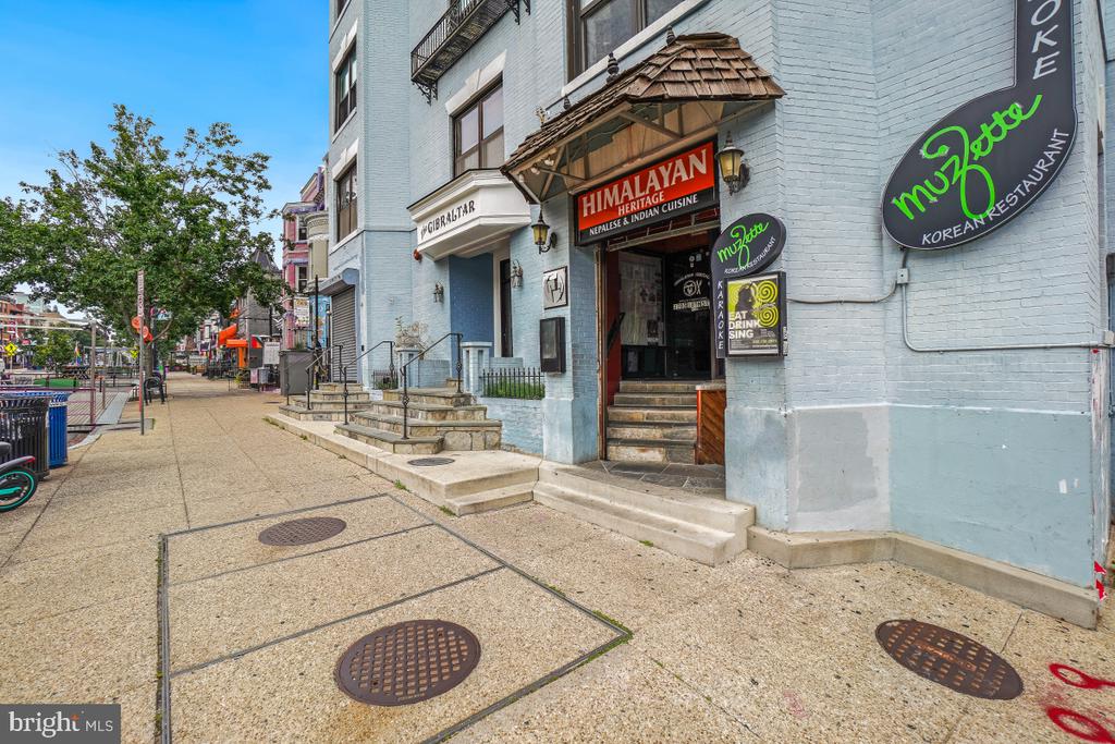 Light blue brick storefront with restaurant signs, entrance steps, and a city sidewalk.