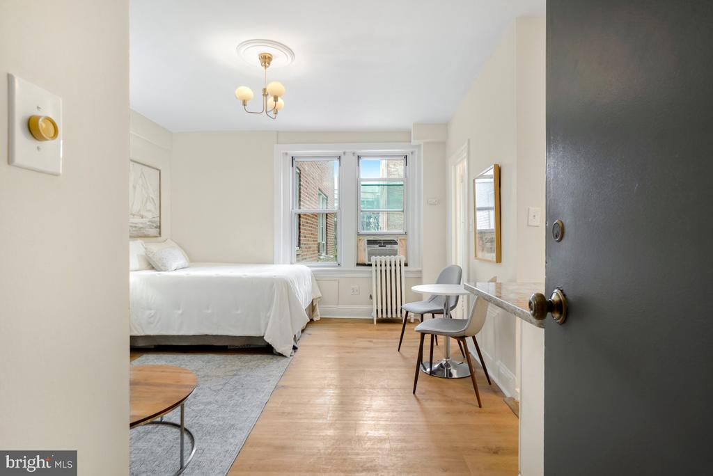 Furnished bedroom with a white bed, two windows, and a small dining area.