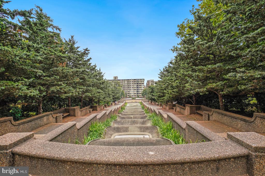 Terraced concrete garden steps framed by mature trees, with an apartment building beyond.