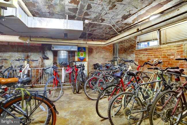 Bicycle storage room crowded with bikes against exposed brick walls and beneath high windows.