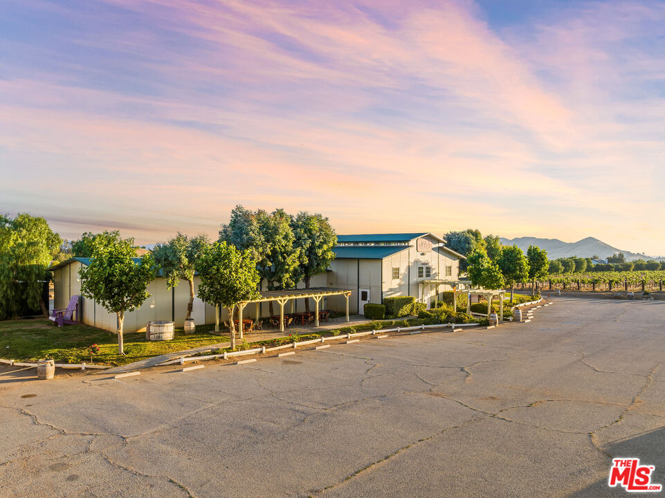 Commercial building beside vineyard rows, with a covered patio and distant hills.