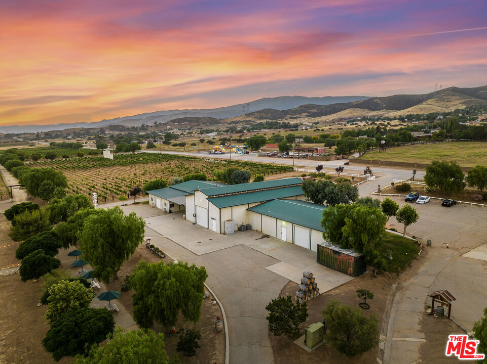 Aerial view of Sierra Highway property with vineyard rows, green-roofed buildings, and mountains at sunset.