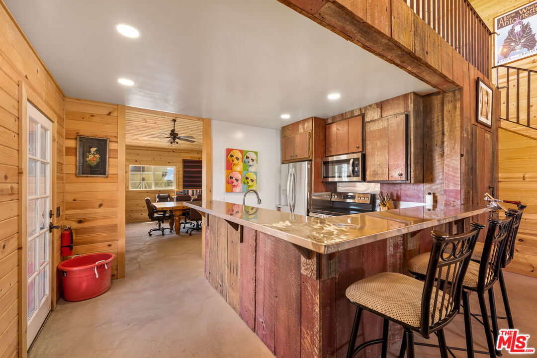 Rustic kitchen with a weathered wood island, stone countertop, and bar seating beside a dining area.