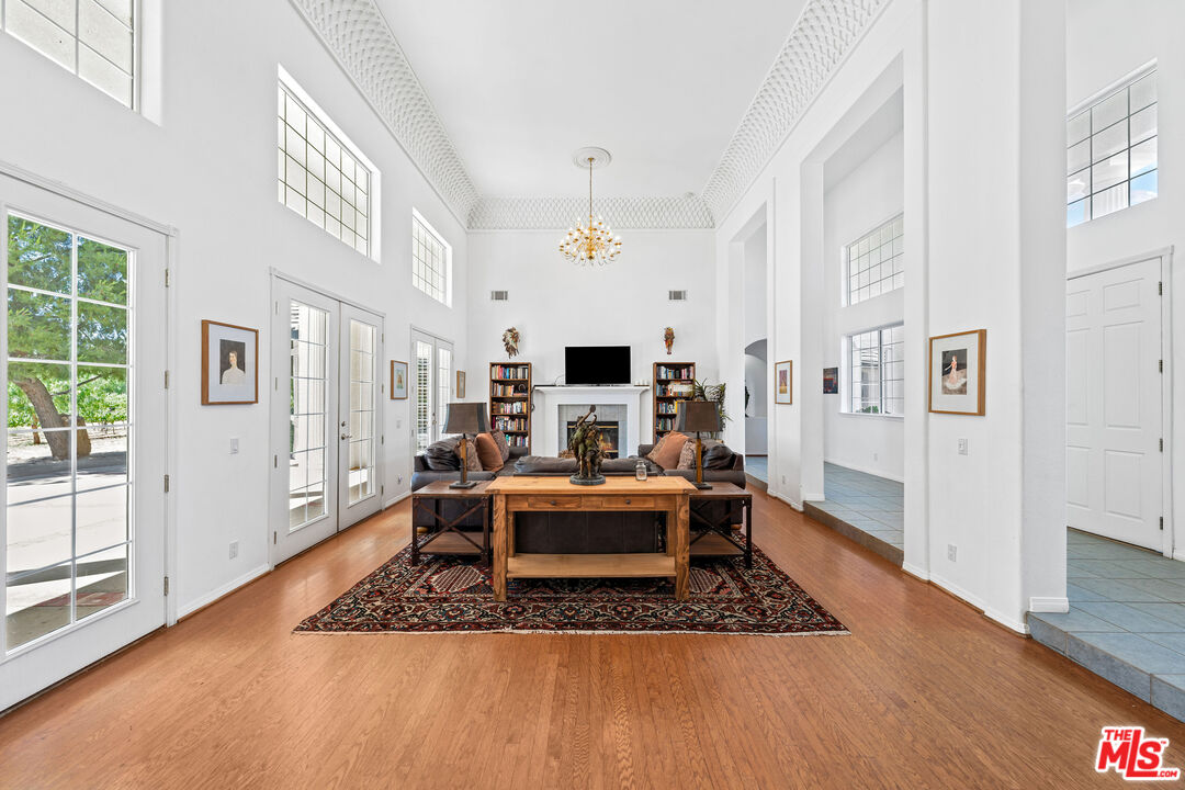 Bright living room with a high ceiling, chandelier, fireplace, and wood floors.