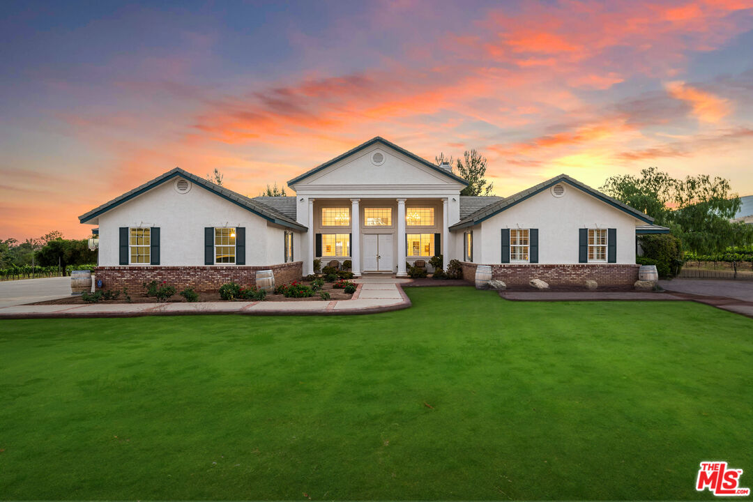 White columned home with brick accents and broad green lawn beneath a colorful sunset.