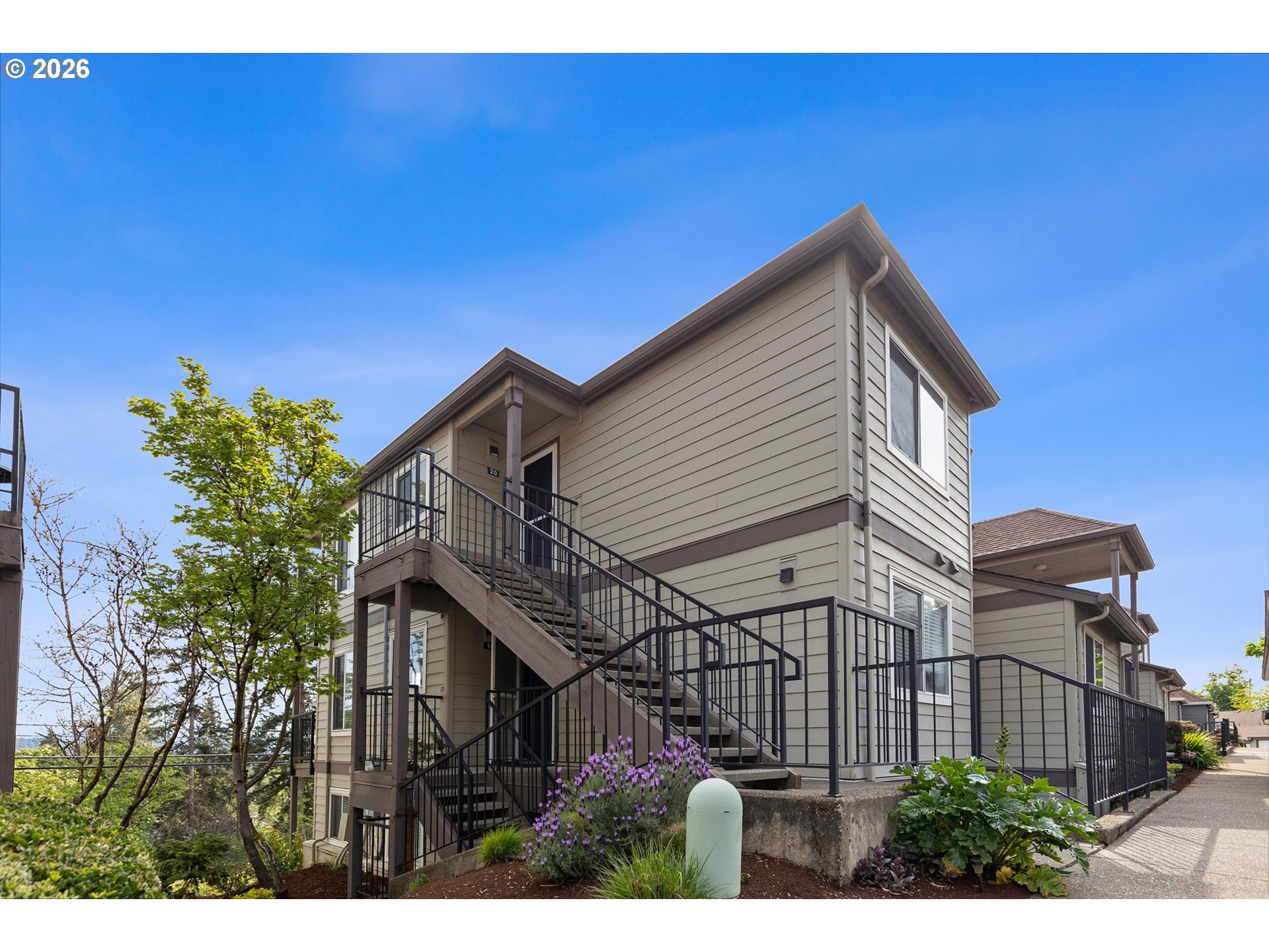 Multi-unit residential building with black-railed stairs and walkways beside landscaped grounds.