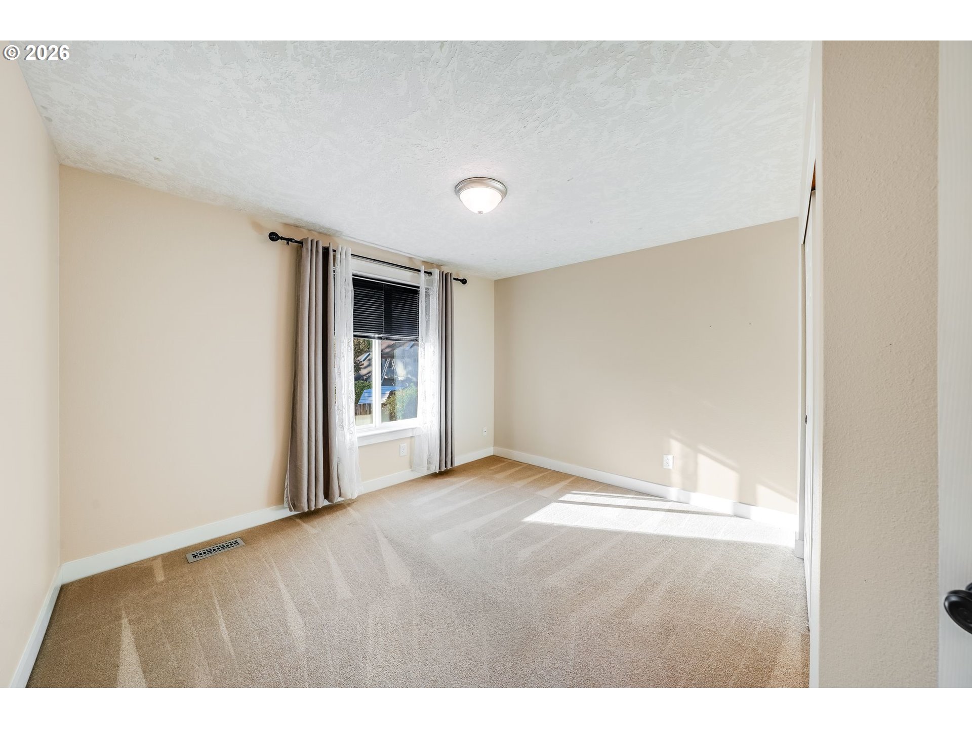 Empty bedroom with tan carpet, beige walls, and a curtained window.