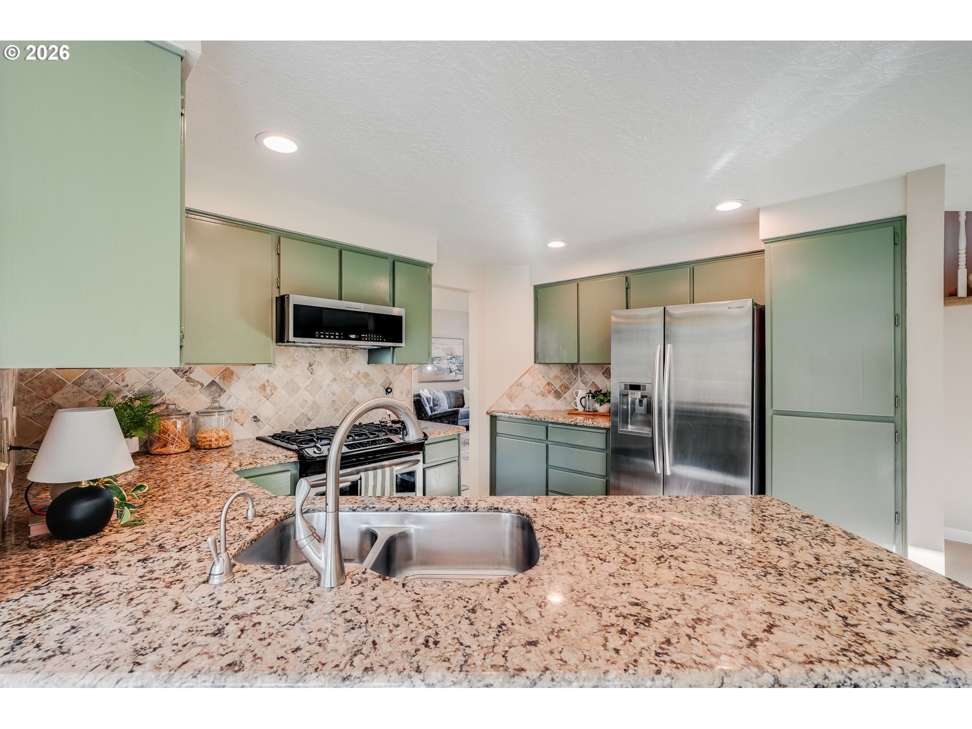 Kitchen with sage-green cabinets, granite island, stainless-steel sink and appliances.