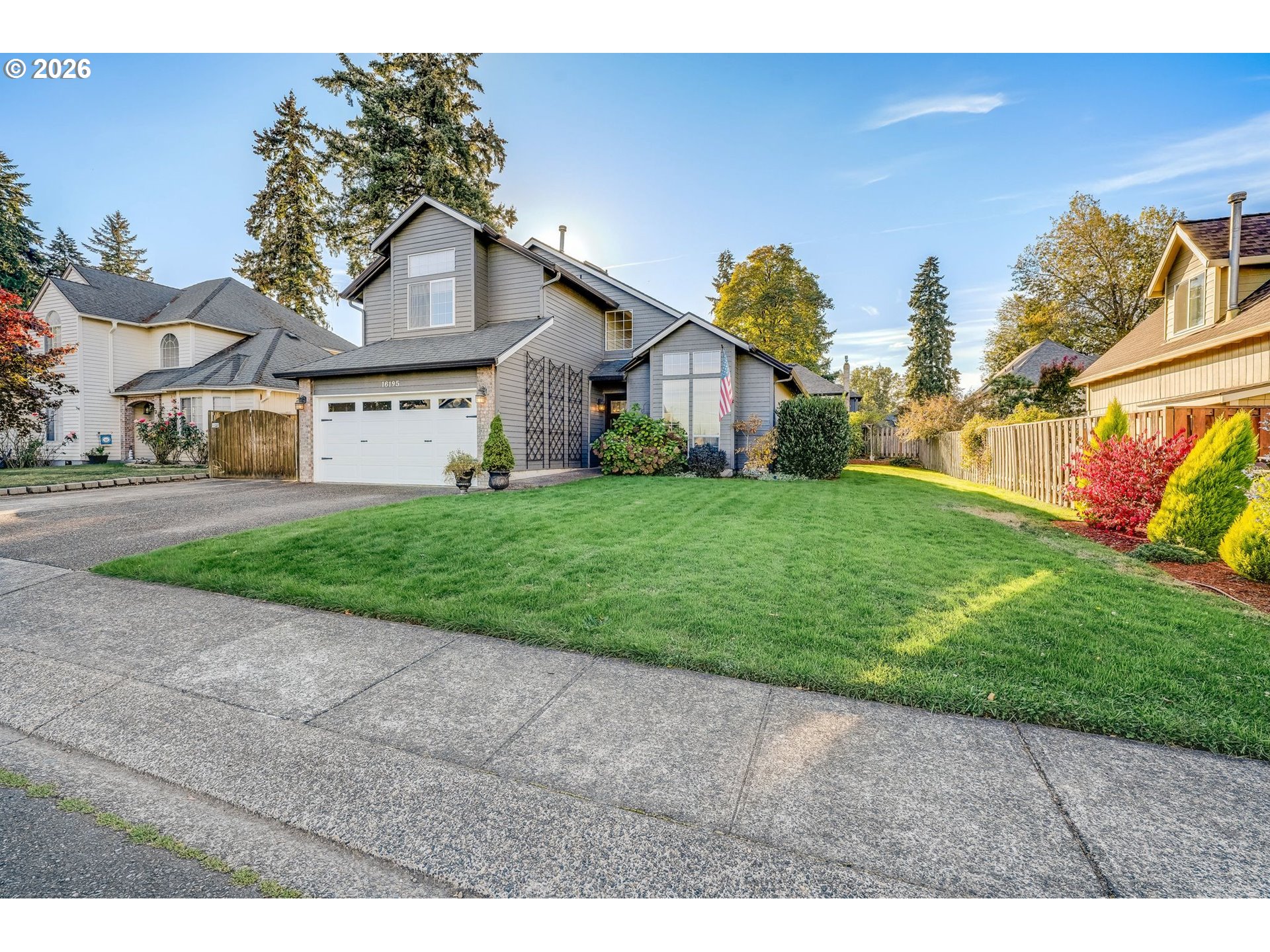 Gray two-story house with a white double garage, landscaped front yard, and broad green lawn.