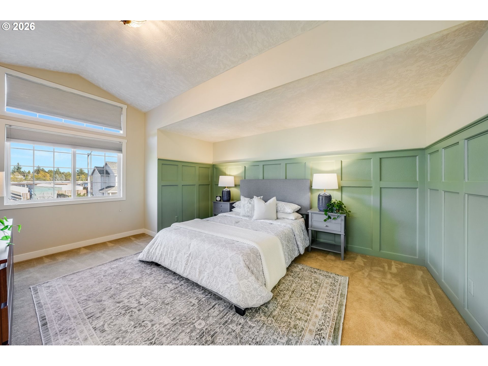Staged bedroom with sage-green paneled walls, a white bed, and large windows.
