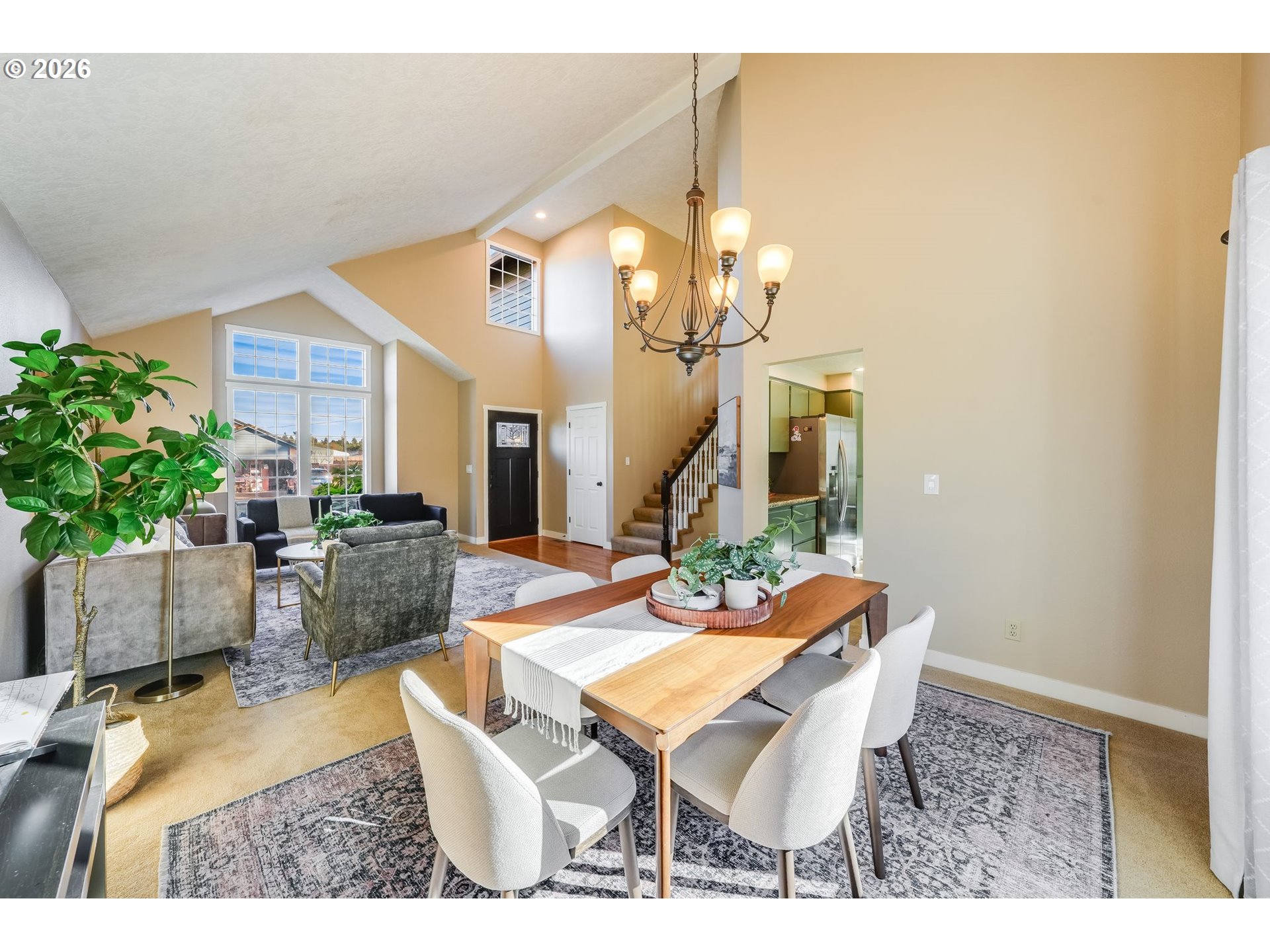 Open-plan living and dining room with a vaulted ceiling, large windows, and a wood dining table.
