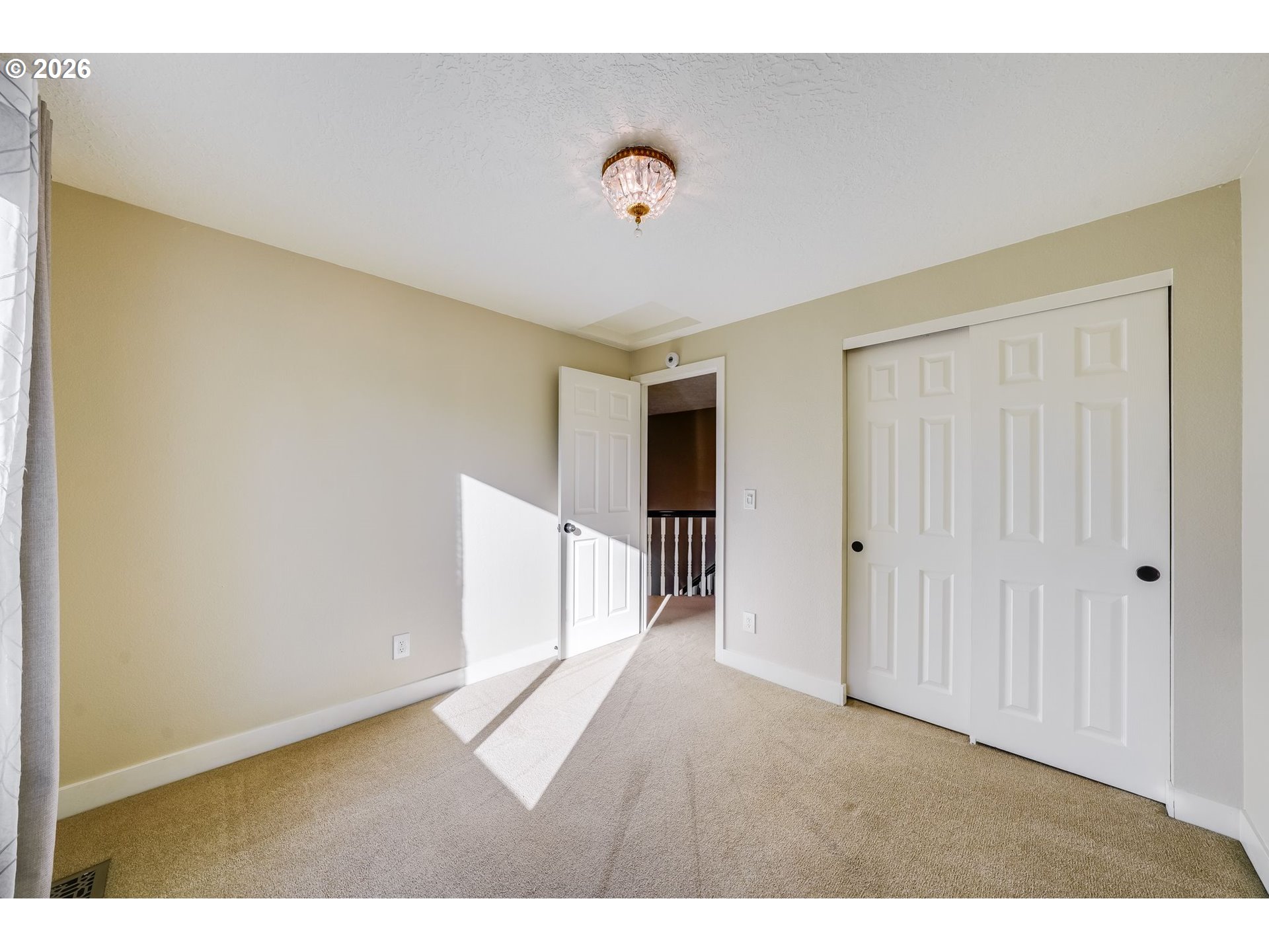 Vacant bedroom with beige carpet, white sliding closet doors, and sunlight across the floor.