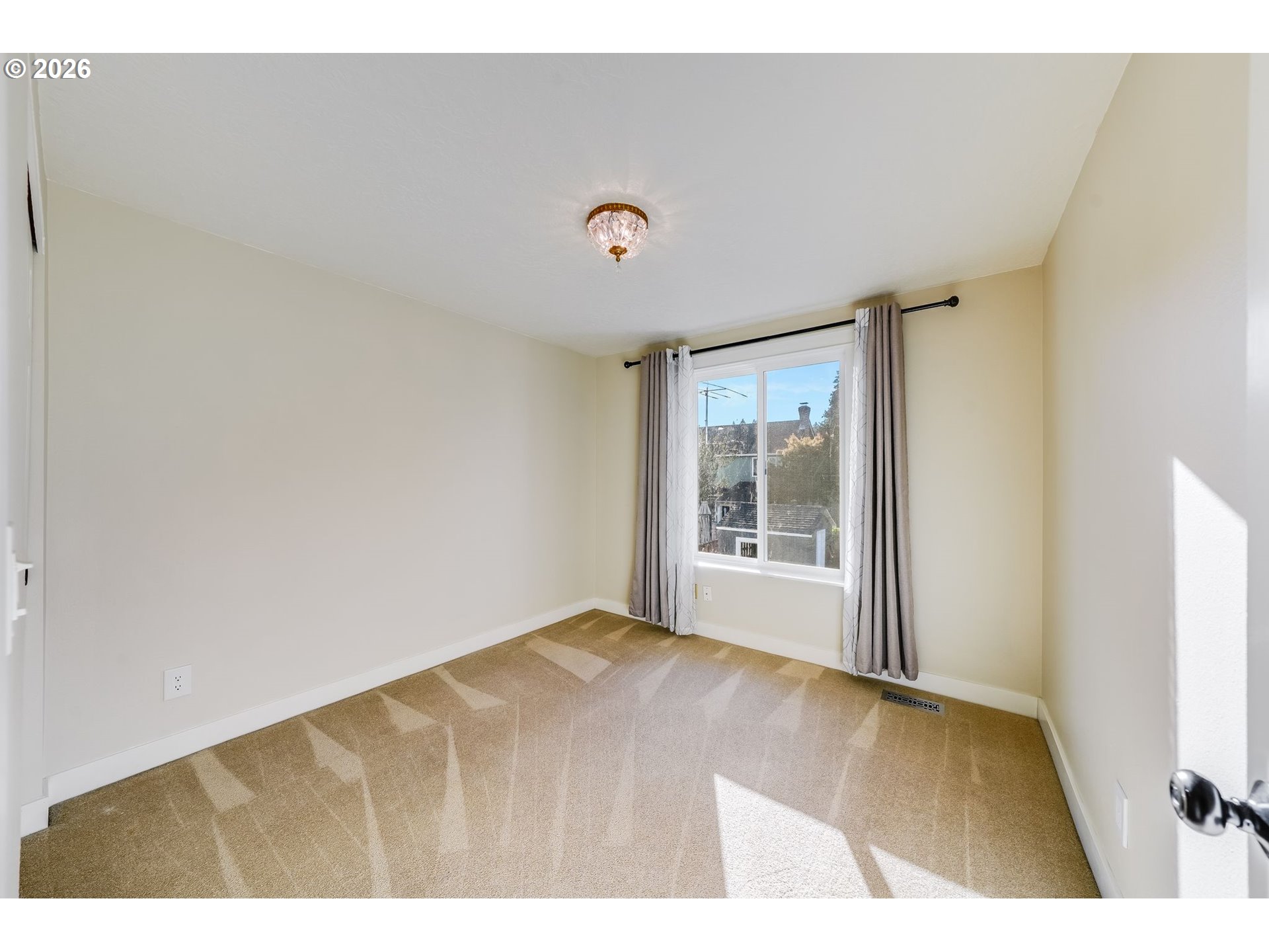 Empty carpeted bedroom with a curtained window and sunlight across the floor.
