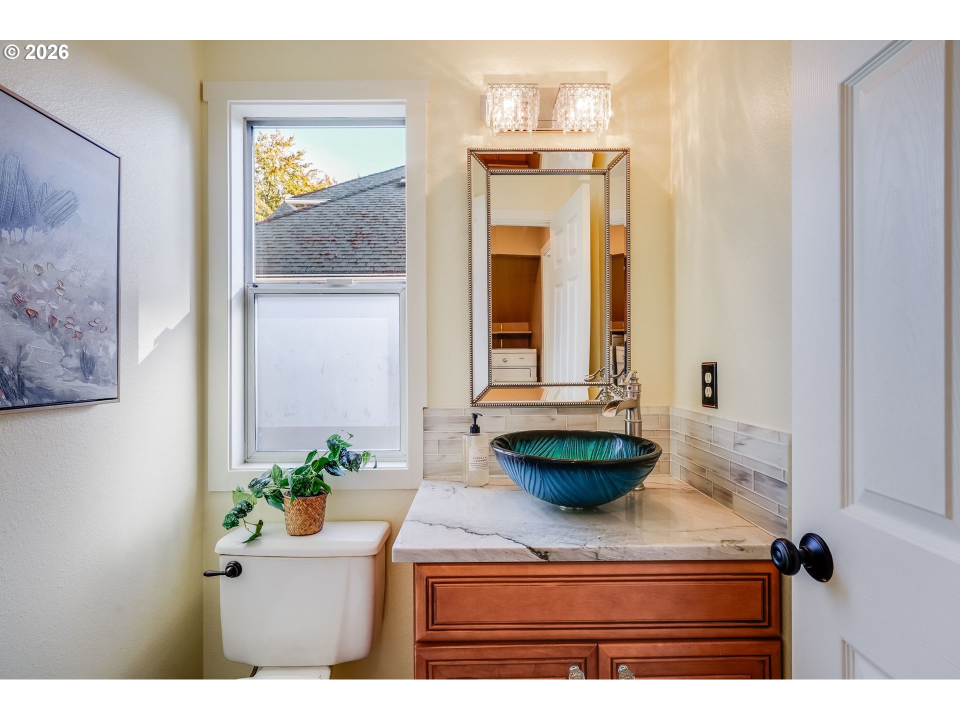 Bathroom vanity with a blue vessel sink, marble countertop, and window beside the mirror.