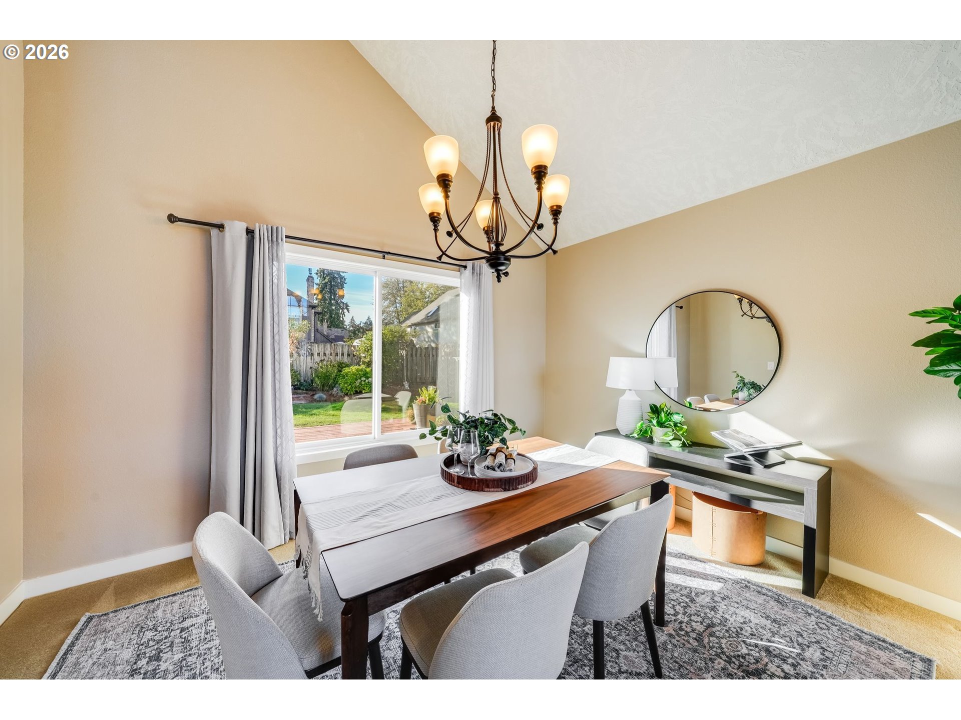 Dining room with a dark wood table, chandelier, and sliding doors overlooking a fenced backyard.