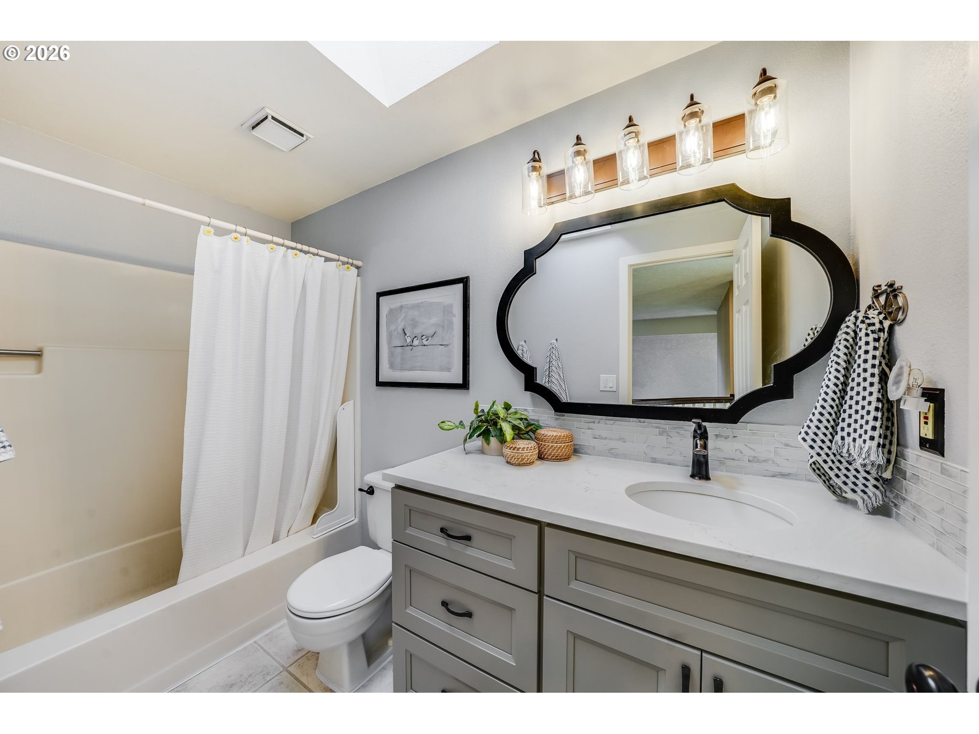 Bathroom with a gray vanity, large black-framed mirror, and bathtub behind a white shower curtain.