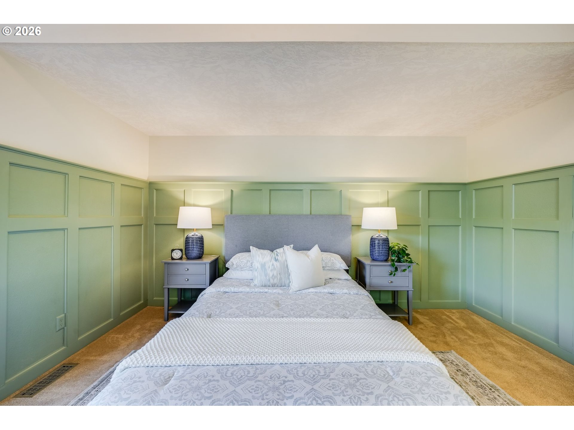 Bedroom with a centered bed, gray headboard, and sage green paneled walls.
