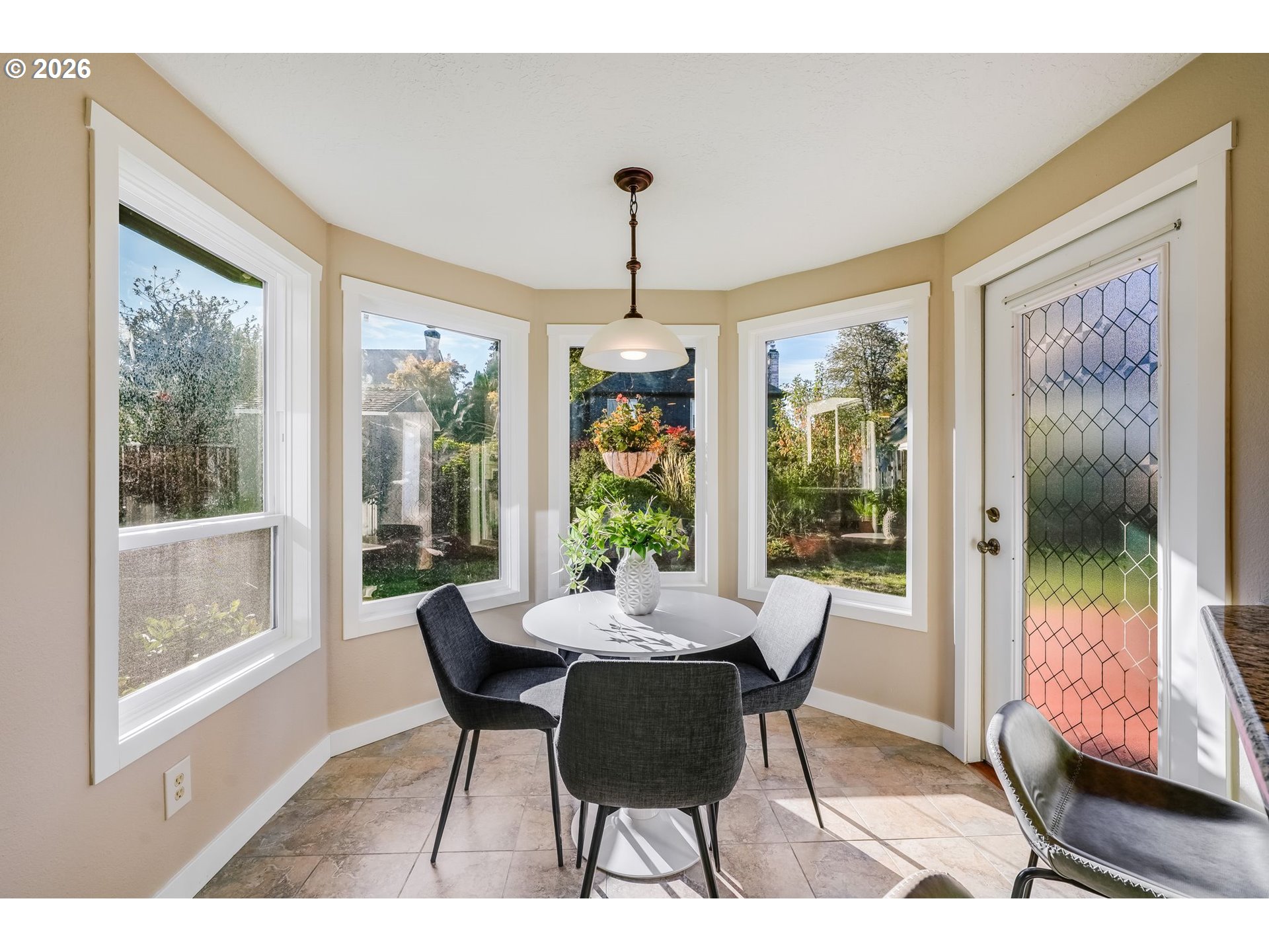 Dining nook with a round table, upholstered chairs, and large garden-facing windows.