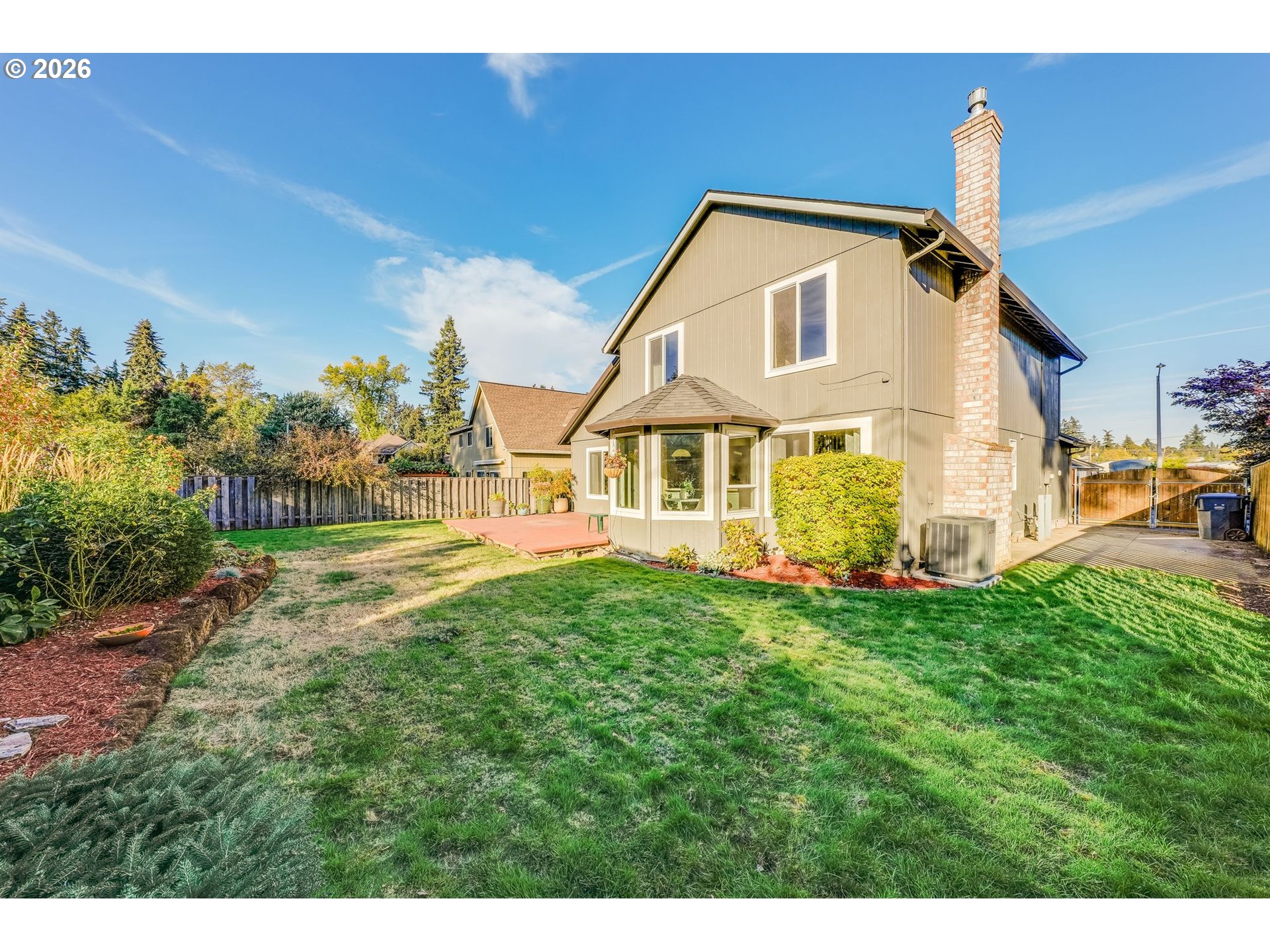 Two-story home’s rear exterior with a brick chimney, bay window, deck, and fenced garden lawn.