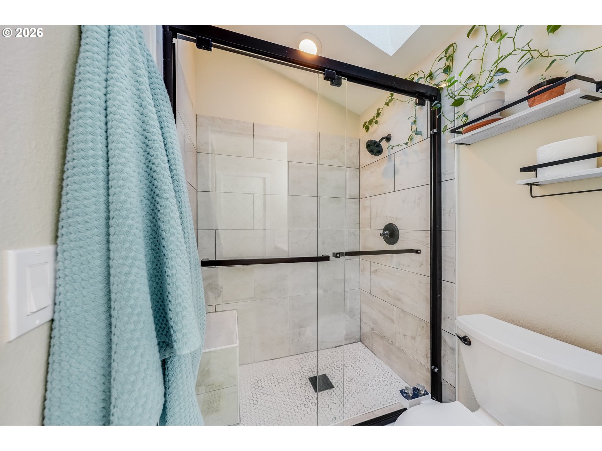 Bathroom with a glass walk-in shower, black fixtures, marble-look tile, and white hexagon-tile floor.