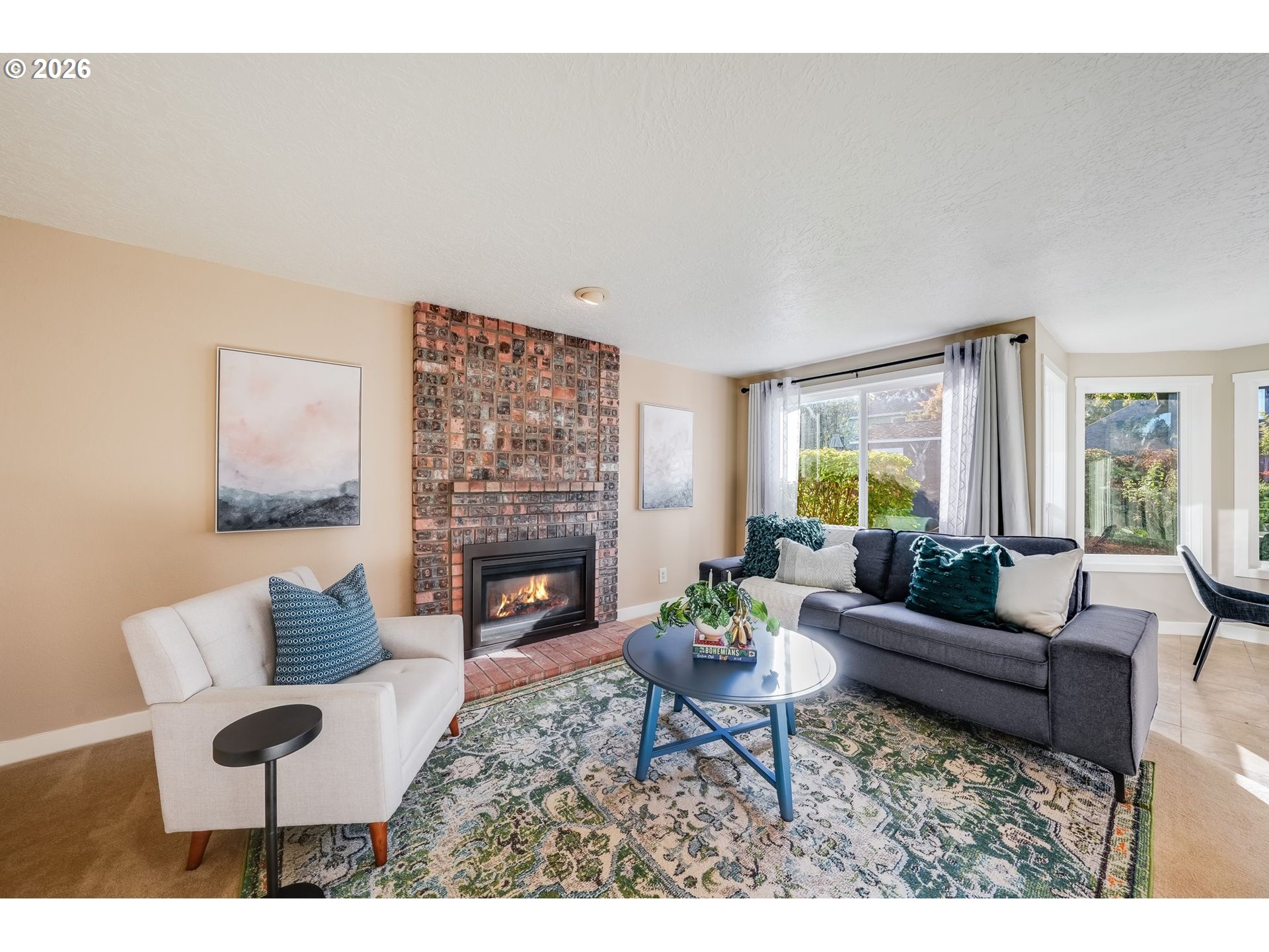 Staged living room with a brick fireplace, contrasting sofas, and large windows.