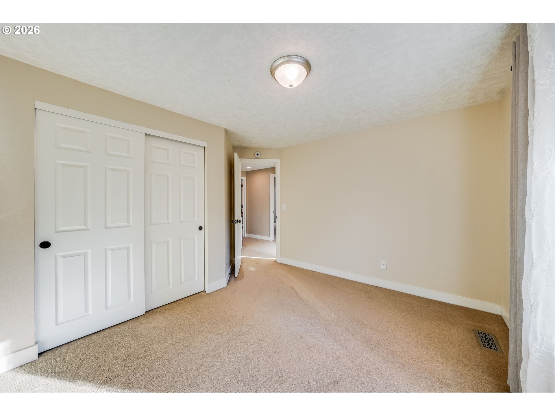 Empty carpeted bedroom with white sliding closet doors and a curtained window.