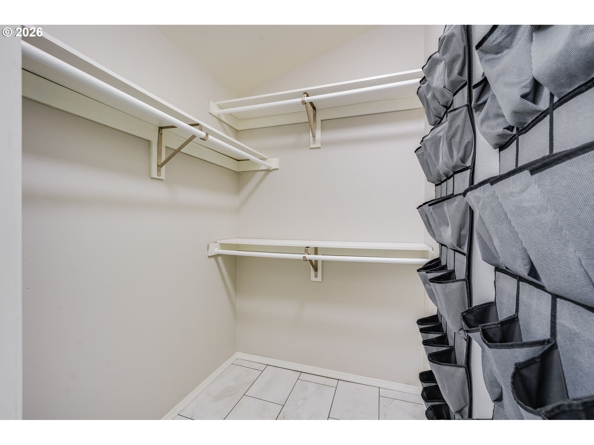 Walk-in closet with multiple hanging rods, gray pocket organizers, and a tiled floor.