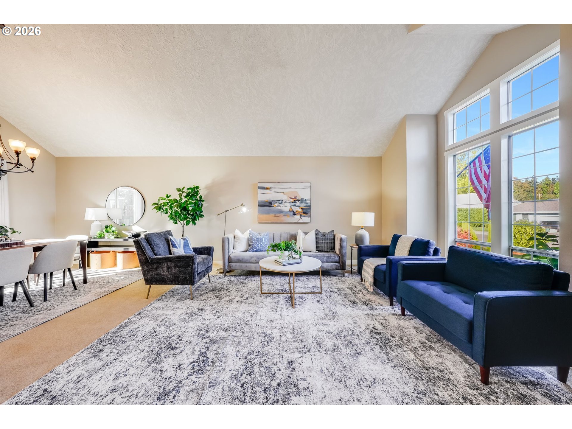 Furnished living room with tall windows, sloped ceiling, gray sofa, and navy chairs.