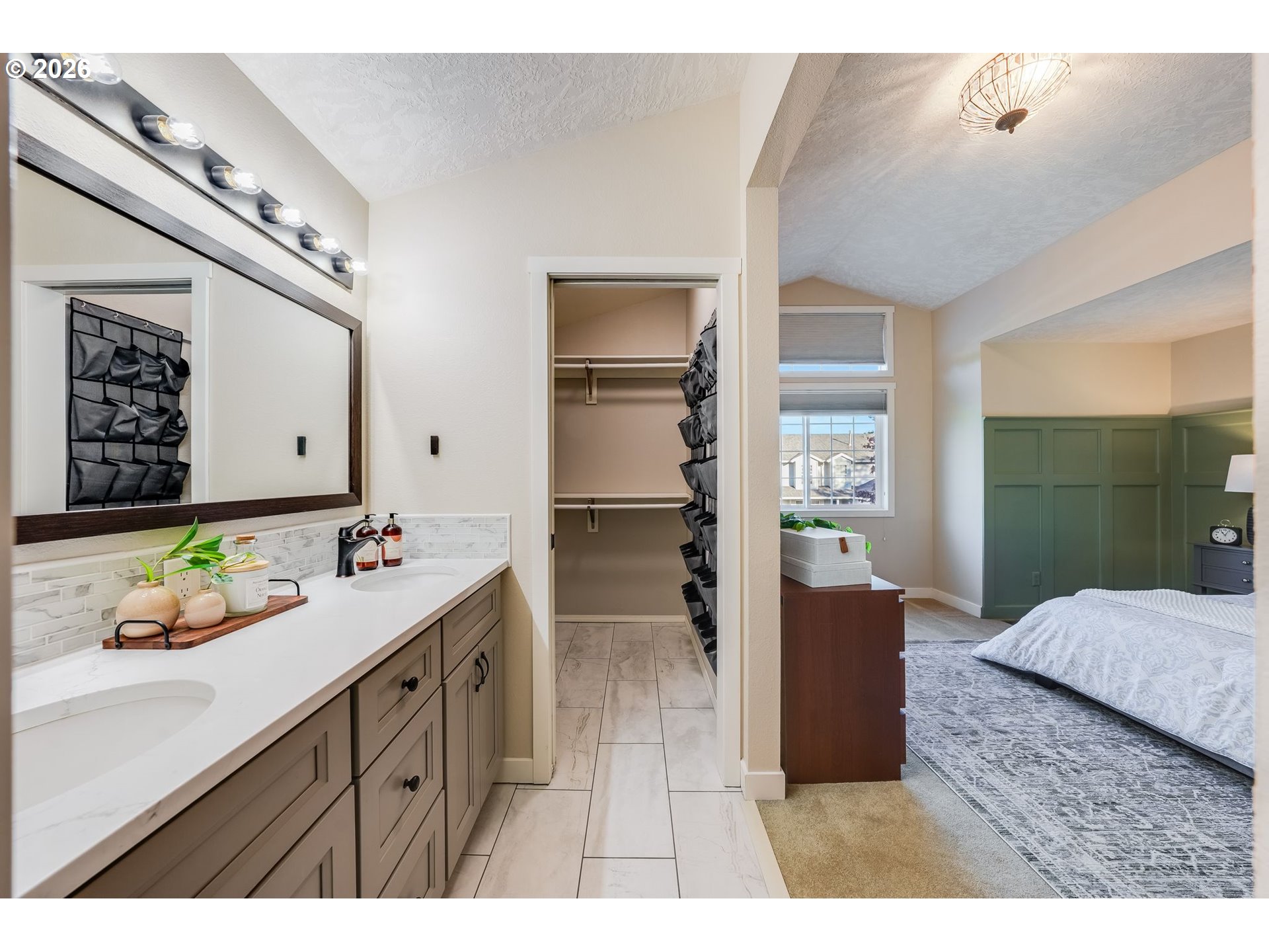 Bathroom vanity with double sinks opens to a walk-in closet and bedroom with green paneled walls.