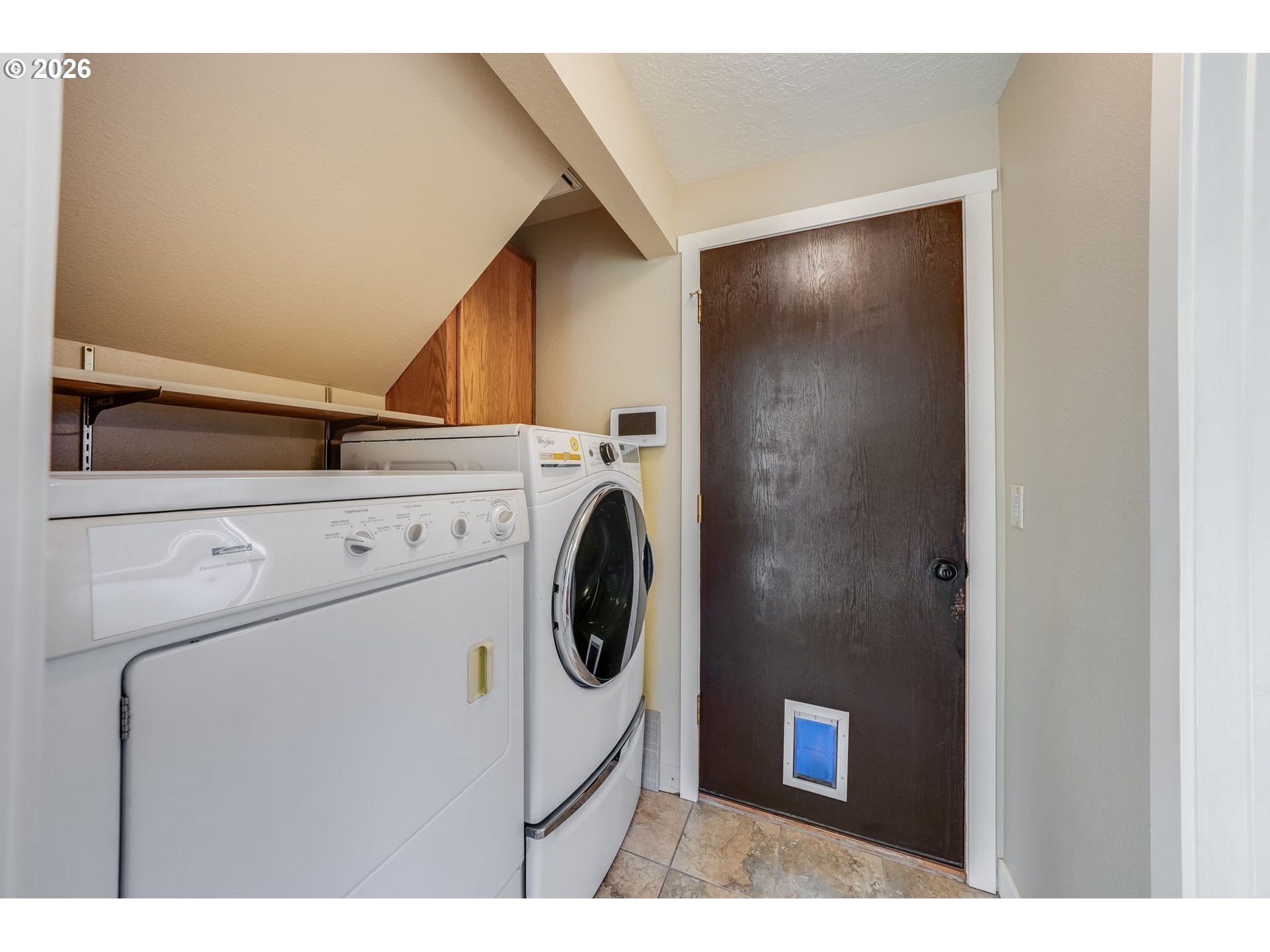 Laundry room with washer and dryer, overhead shelf, and a pet door in the wooden door.