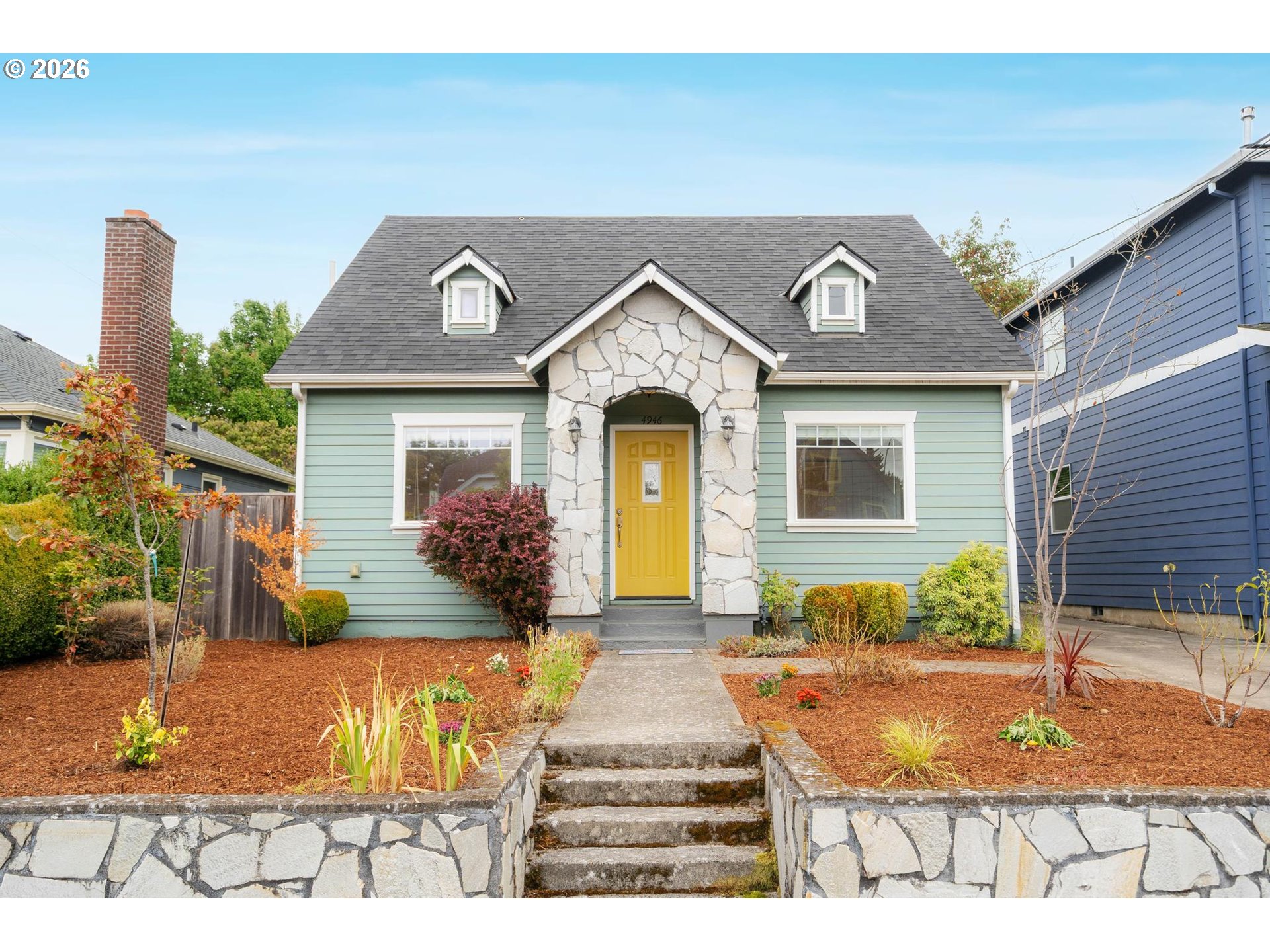 Mint-green house with a stone entry arch, bright yellow door, and landscaped front garden.