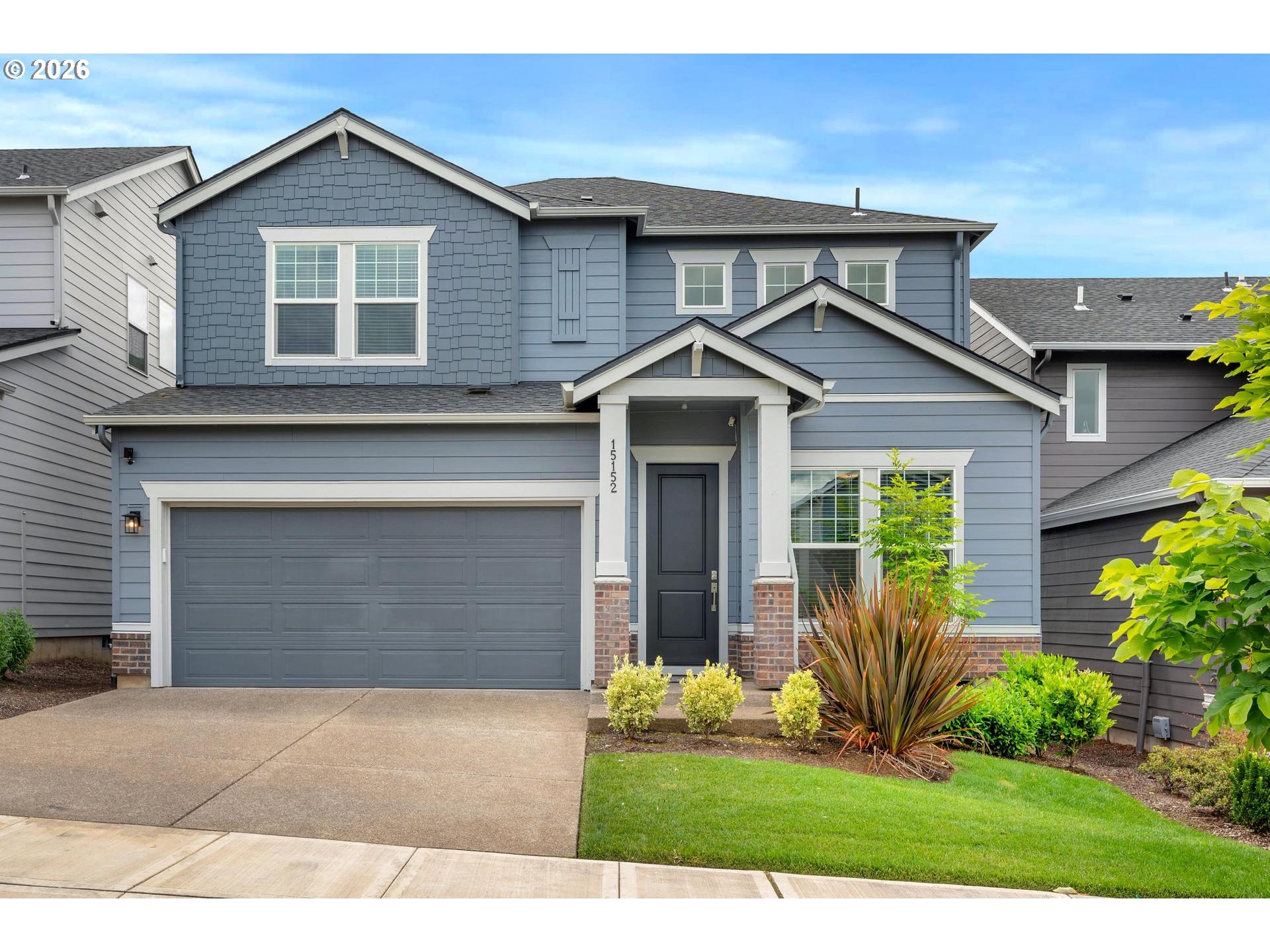 Two-story blue house with a double garage, covered entry, and landscaped front yard.