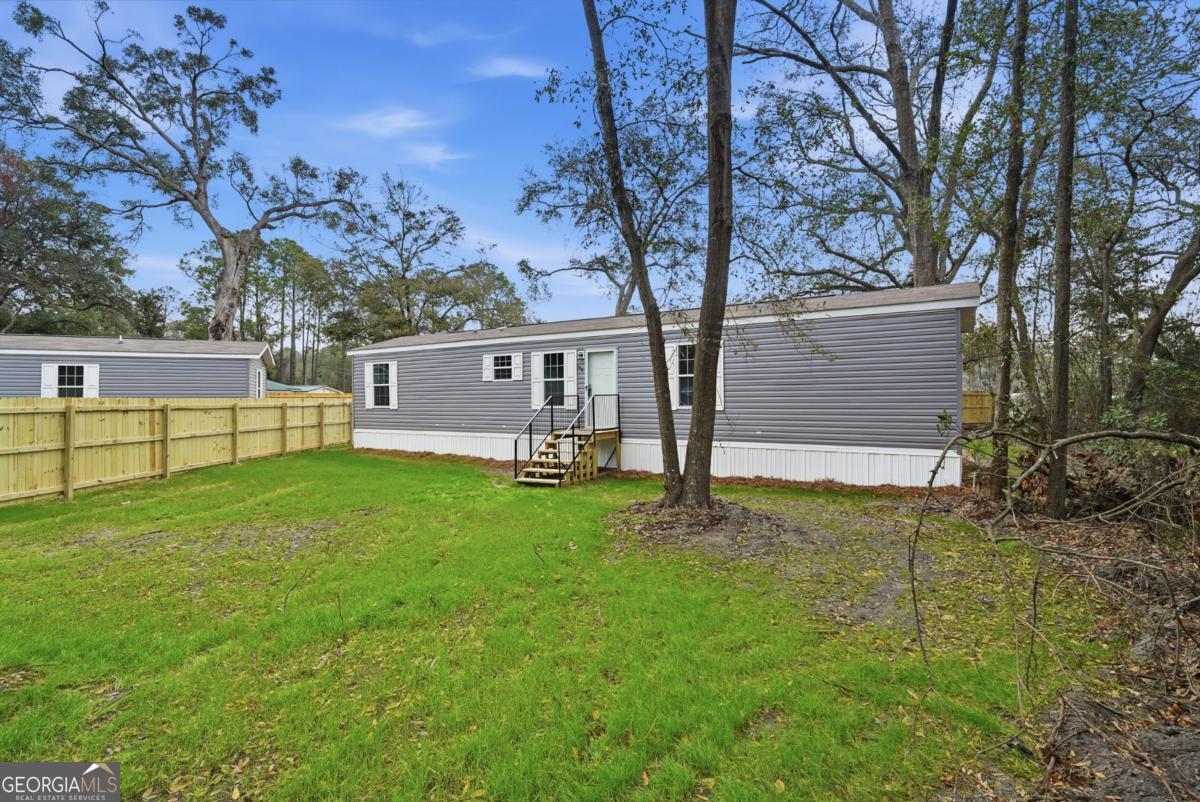 Gray manufactured home with white entry steps in a grassy, tree-lined yard.