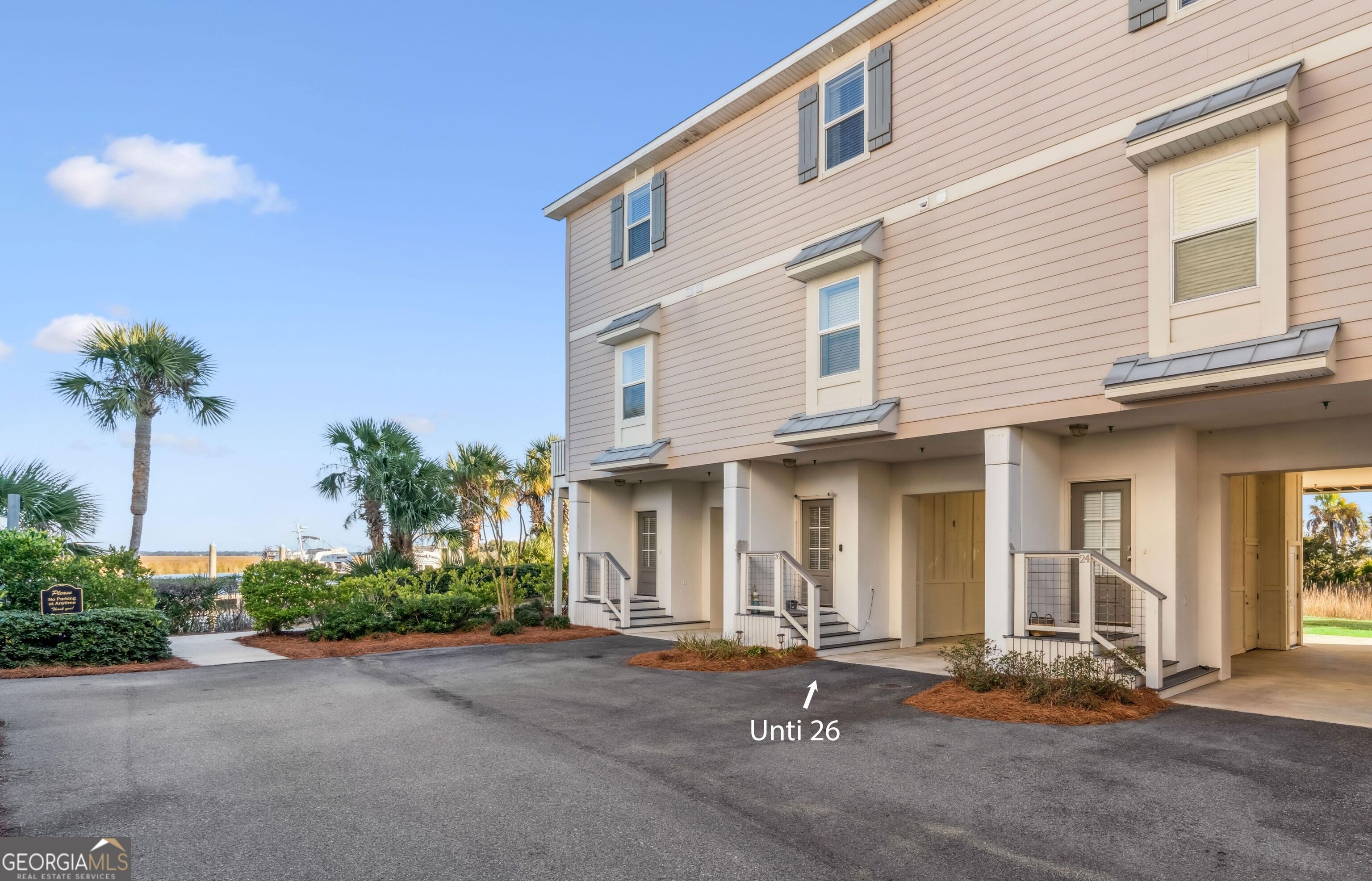 Multi-story townhouse exterior with unit 26 marked, palm trees, and water visible beyond.